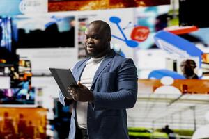 African american professional engaging with media dashboards screens, emphasizes networking with AI and technology. Tech driven person showcases online platforms and internet communication. photo