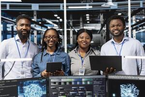 Portrait of happy server farm team looks at data analysis graph to reduce equipment failure. Cheerful data center colleagues look at AI visualization dashboard to pinpoint gear performance glitches photo