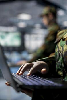 Close up of military server room worker typing on laptop, overseeing firewall configurations. Army information technology specialist in data center deploying software updates in secure facility photo