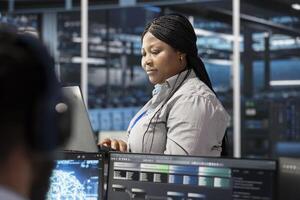 Data center software developer using artificial intelligence neural networks tech. African american server farm employee using AI programming language on computer, configuring specialized hardware photo