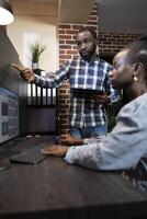 Male and female forex advisors working together at desk, analyzing stock market data on multiple screens late at night. The office features a brick wall and professional workstation. photo