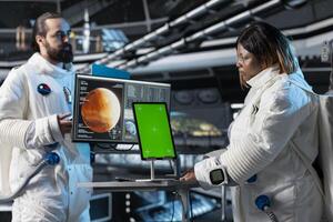 Cosmonauts study mission plans on green screen tablet before Mars expedition, preparing for future of mankind. Astronauts use chroma key device, exploring red planet to support human life beyond Earth photo