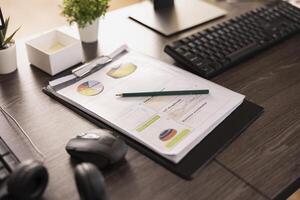 Closeup of an office desk with financial charts, pencil and clipboard. A keyboard, mouse and small plants add to the modern workspace, highlighting business analysis and productivity. photo