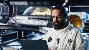 Astronaut using laptop to verify mission parameters after completing planet surface expedition. Cosmonaut manages systems using notebook, leaving Mars, updating flight log to return home photo