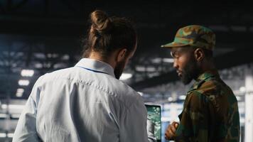 Military technician reviewing tactical dashboard on laptop screen inside secure server hub. Army expert using strategic communications and infrastructure oversight software on notebook photo
