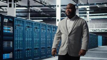 Smiling engineer in server hub monitoring data center energy consumption across components. Happy IT expert walking in data center, making sure rigs sensors are functioning optimally photo