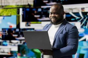 African American user emphasizing visual concept of online communication, connecting to web platforms and apps. Mobile technology surrounded by social network icons in a digital space. photo