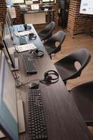 Vacant collaboration space in modern office, featuring multiple desks, digital monitors and headsets, ideal for customer support team. Empty table neatly organized with devices for group of employees. photo