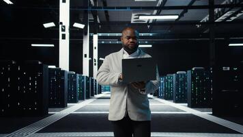Data center system administrator coding on laptop, doing software updates. Server room IT specialist looking at device screen, optimizing infrastructure rackmounts configuration rigs, camera A photo