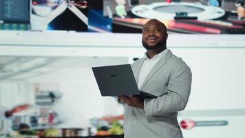 Smiling person uses laptop, enjoying leisure time with content on streaming services. Joyful man watches media VOD broadcasts on notebook in front of digital backdrop filled with clips, camera A photo
