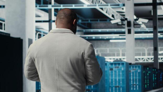 empleado caminando en servidor granja, analizando equipo métrica en dispositivo pantalla. africano americano datos centrar ingeniero haciendo análisis en tableta utilizando datos reunido por infraestructura plataformas, cámara si foto
