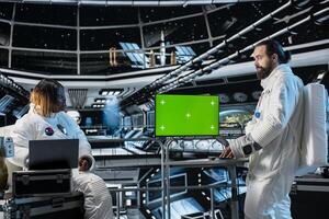 Astronauts wearing spacesuit in futuristic spacecraft monitoring mission data on chroma key screen. Spaceship crew prepares for space travel operations, reading data on isolated screen mockup monitor photo