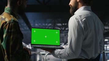 Army tech specialist in data center and coworkers using green screen laptop to troubleshoot military computer systems. Soldier and command center server room admins using chroma key notebook photo