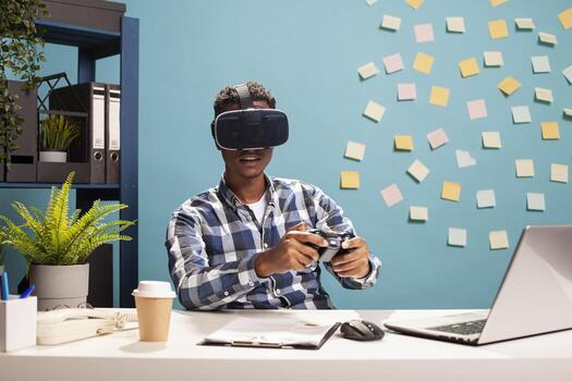 Research team leader using a modern gamepad, enjoying games at his desk. Black businessman gaming with a console controller, wearing VR headset for advanced interactive experience. photo