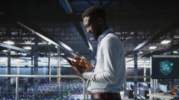 Technician walks in data center, doing maintenance tasks on tablet, ensuring optimal performance. IT expert reviewing diagnostics and applying patches to server hub gear, improving stability, photo