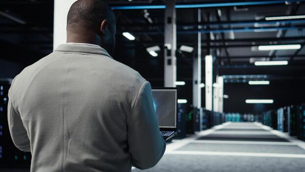 Server room admin using laptop to do infrastructure AI machine learning automatization. Software developer walking in data center doing maintenance using artificial intelligence, camera A photo