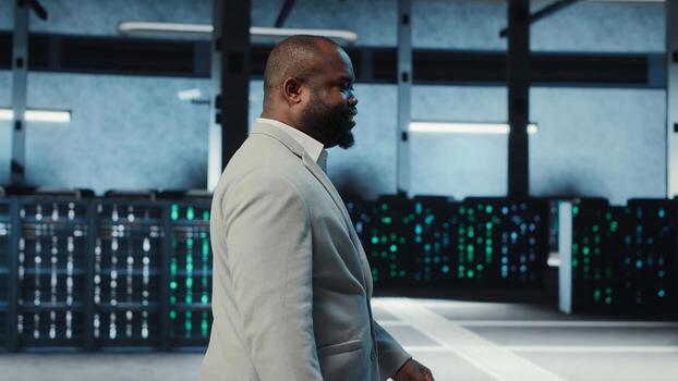 Employee walking in high tech data center with hardware used to host websites. IT professional overseeing dimly lit server farm setup helps companies stay connected, camera B photo
