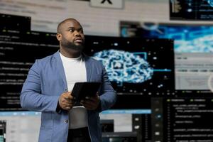 Black software expert focusing on programming language for innovation, reading binary code on terminal window. Reviews code development for data science. Modern futuristic coding life. photo