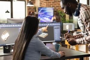 Asian woman manager pointing to screen, providing a crash course training to her male employee. Black man standing with a clipboard, taking notes as female developer explains the cad software. photo