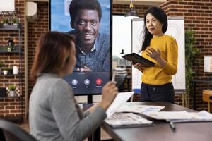 Businesswomen collaborating on startup project, utilizing led screen for a call with an african american client. Female coworkers in virtual meeting with male manager, providing company updates. photo