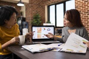 Financial expert advising an investor on market trends, examining the charts on laptop. Business female analysts collaborate on financial reports, reviewing company analytics data on device screen. photo