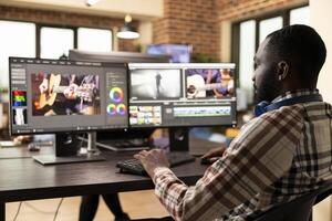 African american filmmaker working on a high quality project, refining visuals and enhancing audio on his desktop monitors. Black man using advanced editing software in modern production office. photo
