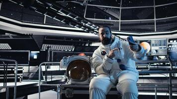 Astronaut doing hand gestures while taking selfies with smartphone inside space station during exploration mission. Man takes pictures with mobile phone during cosmic expedition photo
