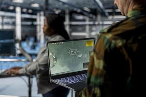 Close up of military officer in data center looking at missile lock interface displayed on laptop screen. Soldier in army server hub checking target coordinates and crosshair overlay on notebook photo