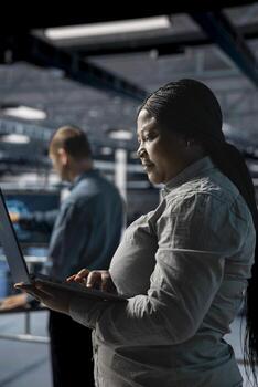 Server farm colleagues working together, running diagnostics on infrastructure using laptop. Teamworking data center engineers deploying new builds to improve uptime using notebook photo