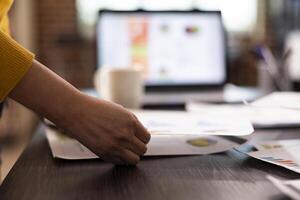 Selective focus on a person holding a paper at an office desk filled with research paperwork. Closeup of hand of an individual grasping a business document on table in modern workspace. photo