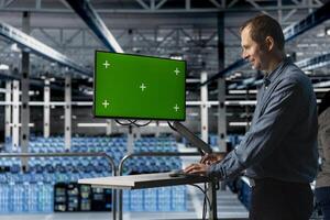 Cheerful IT server room expert uses chroma key computer to minimize hardware downtime. for increased storage capacity. Jolly data center engineer using green screen PC to automate anomaly detection photo