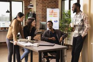 Multiethnic professionals in a startup office takes a break, enjoying a moment of laughter. Caucasian woman with hands clasped tells a funny story to her diverse colleagues at desk. photo