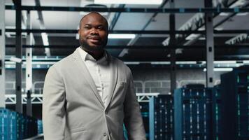 Smiling engineer walking in data center, checking hardware for system stability. Happy employee overseeing server farm, configuring infrastructure to optimize performance, camera B photo