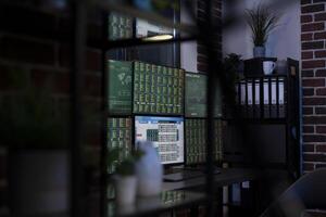 Dimly lit office at night with multiple screen displaying forex trading charts, anticipating arrival of employees for the upcoming trading session in high tech financial workspace. photo