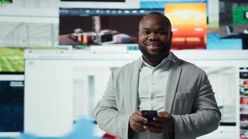 Portrait of cheerful man browsing social media feed on smartphone in front of digital wall. Happy person using mobile phone, floating icons highlight interactive engagement online, camera A photo