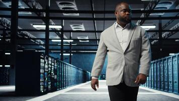 Admin working in high tech server hub capable of processing and storing vast amounts of data. African american IT specialist troubleshooting server rows controlling network resources, camera A photo