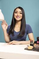 Closeup of asian female vlogger waving hello to her channel subscribers during a live stream. Young woman sitting at desk with a smile, recording a with warm greeting gesture towards the camera. photo