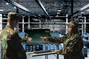 Army soldiers in data center using digital crosshairs to lock onto enemy targets. Military units in server hub command room looking at tactical software screen on monitor photo