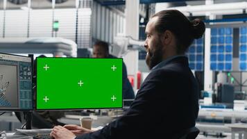Young business specialist uses computer with green screen and production metrics, overseeing the industrial operations and high tech equipment. Master engineer works on sustainability. Camera B. photo