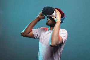 Black male model playing an interactive VR game, engaged in a futuristic 3D simulation, adjusting his headset. African american man looking upward and exploring a virtual reality world. photo