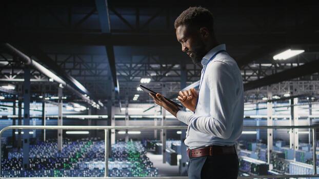 Admin on data center industrial platform analyzing infrastructure performance outputs on tablet. Server room employee doing job tasks, finetuning mainframes configurations, photo