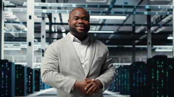 Smiling manager in data center doing checkup on hardware to avoid downtime. Happy african american supervisor overseeing server room infrastructure supercomputers, camera B photo
