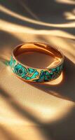 Gold ring with teal floral inlay, sunlit photo