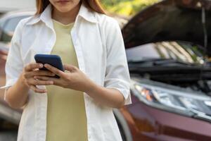 breakdown, broken car, Woman uses mobile phone check insurance premiums through application due to car accident . Find garage to get car fixed during country tour, waiting for help, emergency. photo