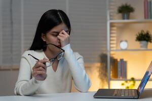 Eye problems, Asian women with tired and irritated eyes, eye rubbing, dry, eye pain after work, migraine, headache, blurred vision, photophobia, working in the dark, blue light from computer screens photo