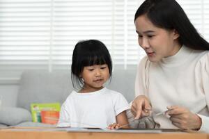 Happy Asian mother relax and read book with baby time together at home. parent sit on sofa with daughter and reading a story. learn development, childcare, laughing, education, storytelling. practice. photo