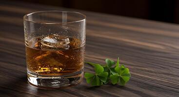Glass of Whiskey with Ice and Green Clover on Wooden Tabletop photo