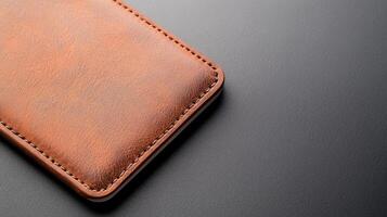 A brown leather phone case rests atop a sleek dark surface, showcasing its quality design and craftsmanship with fine stitching details photo