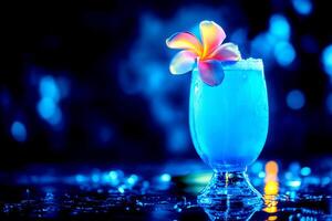 A captivating blue cocktail adorned with a vibrant flower sits on a shiny surface, glowing amidst an enchanting dark backdrop photo