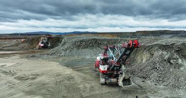 Excavator mining ore in open pit mine under cloudy sky. Stock clip video